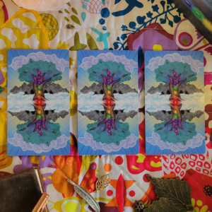 Three cards from Chakra Healing Tarot are placed face-down on a colourful quilted surface. There is a journal, pen and charms on the table as well.
