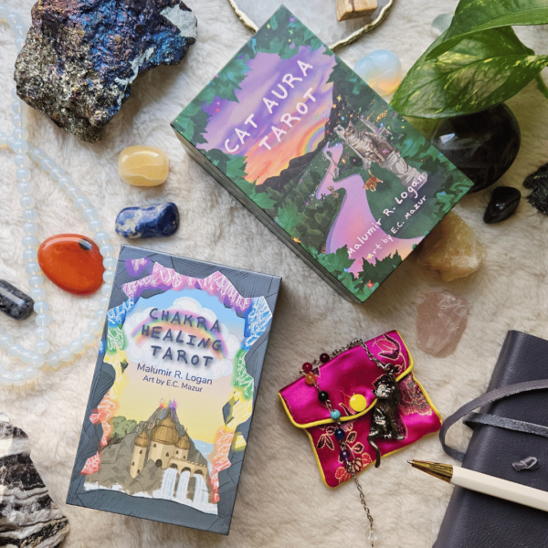 Flatlay of Chakra Healing Tarot and Cat Aura Tarot boxes on a fluffy cream surface, surrounded by crystals, a plant, a journal, pen and a cat-shaped pendulum.