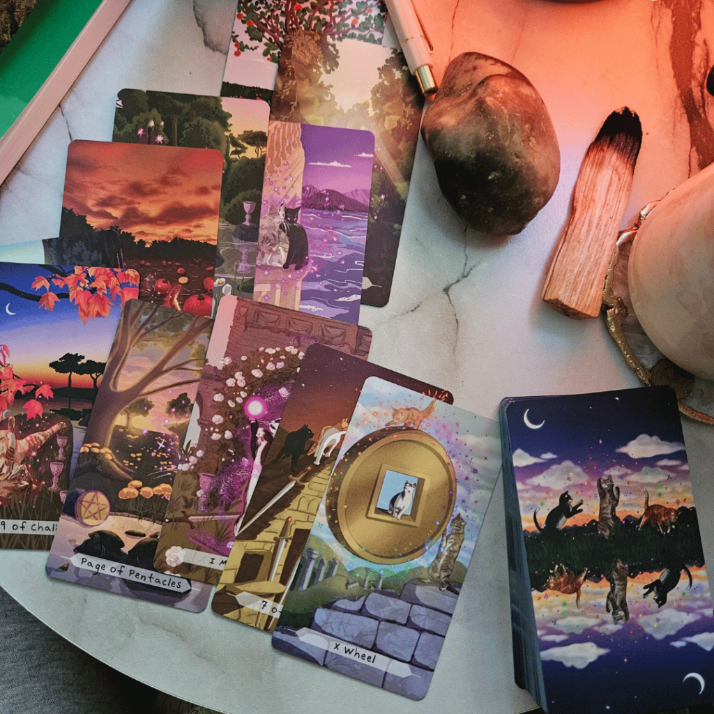 Several cards are laid in a somewhat messy style on a table. Cards are from Cat Aura Tarot which depicts cats in colourful settings in the RWS style Tarot tradition.